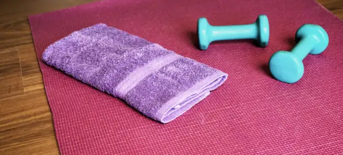 Pink yogamåtte med lilla håndklæde og to turkise håndvægte på et trægulv